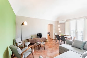 Un salon comprenant un canapé, des fauteuils, un téléviseur, une petite table et une lampe.