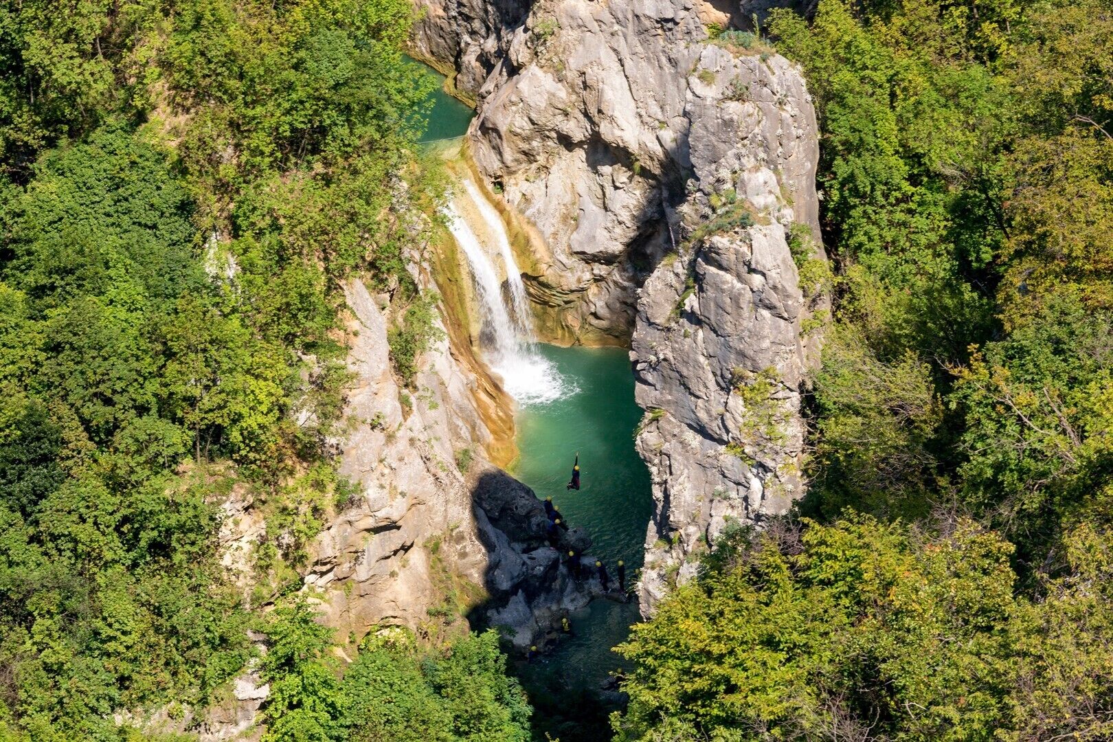 Vista aérea de una formación rocosa natural con una cascada y una poza de agua en su base.