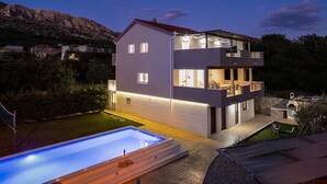 Ein modernes, zweistöckiges Haus mit Swimmingpool, überdachter Terrasse und Blick auf die Berge.