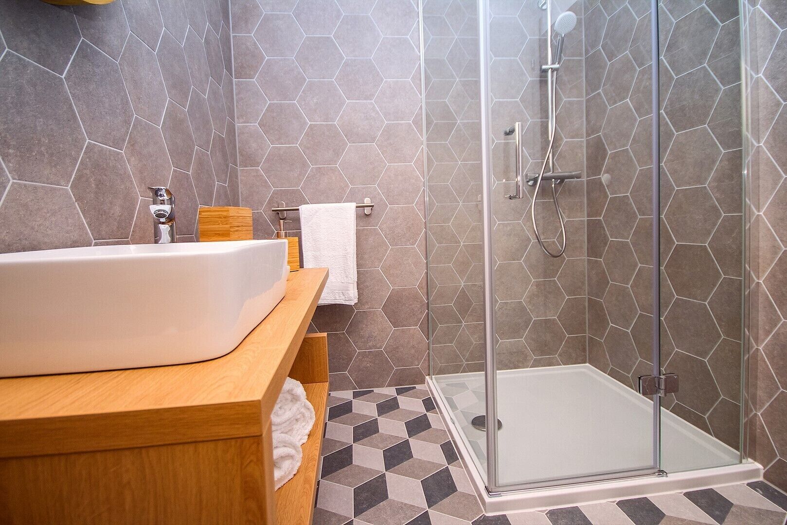 A bathroom with a glass-enclosed shower, a wooden vanity, and hexagonal patterned tiles.