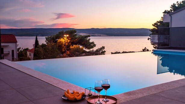 Blick auf einen Pool im Abendlicht, ein Tablett mit Gläsern und einer Schale, und ein Gebäude im Hintergrund.