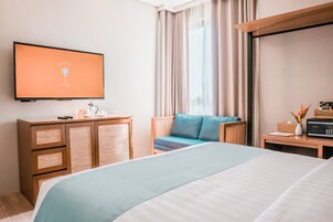 Una habitación de hotel moderna con una cama, un televisor montado en la pared, un aparador de madera, una silla de mimbre y una mesita de noche con una radio.