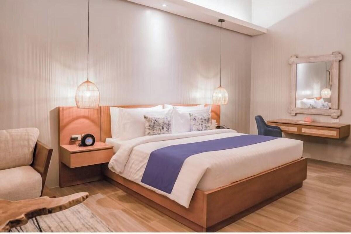 A modern bedroom with a large bed, bedside tables, a chair, a mirror, and a wooden floor.