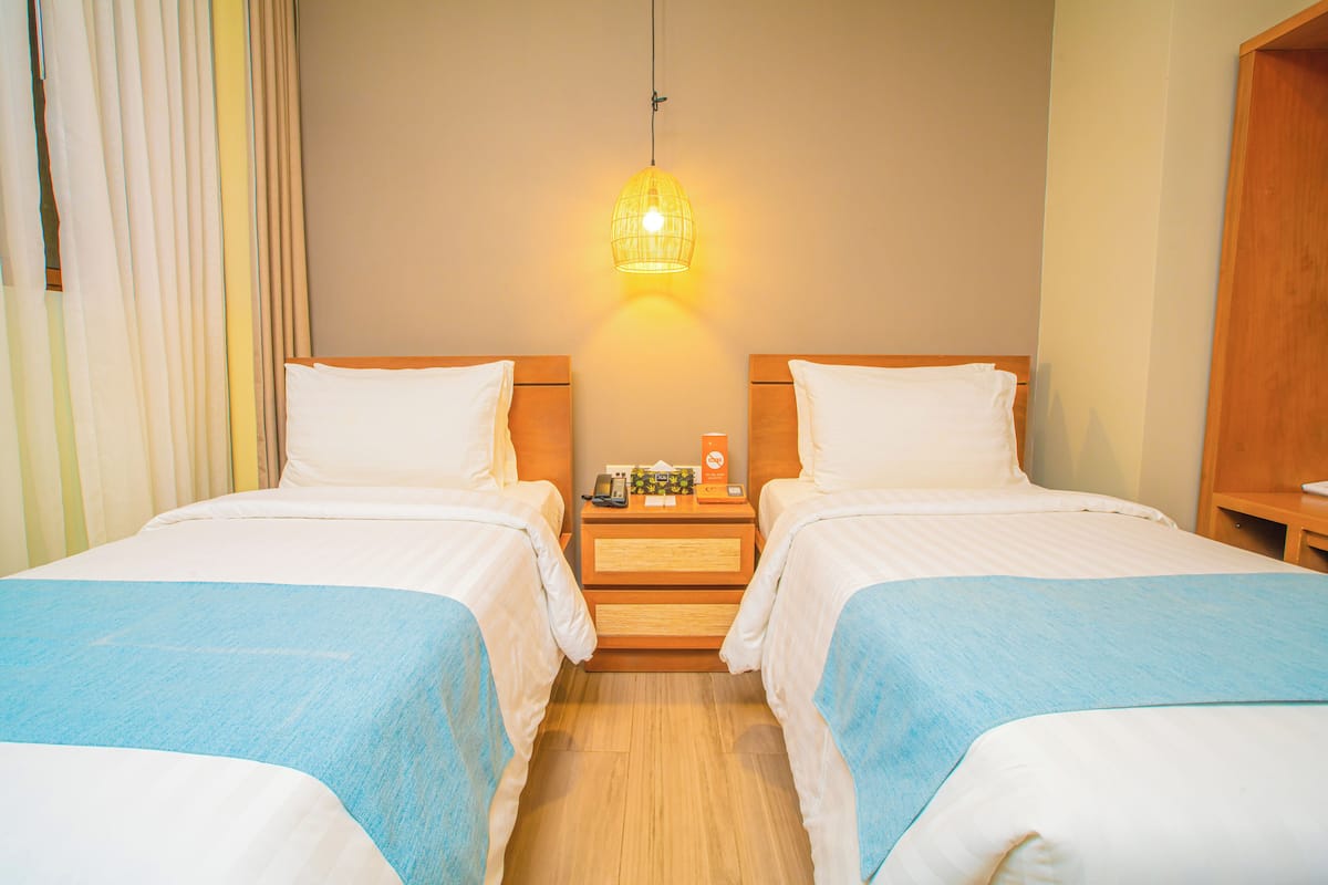 Una habitación de hotel con dos camas, una mesita de noche con lámpara y un armario de madera.