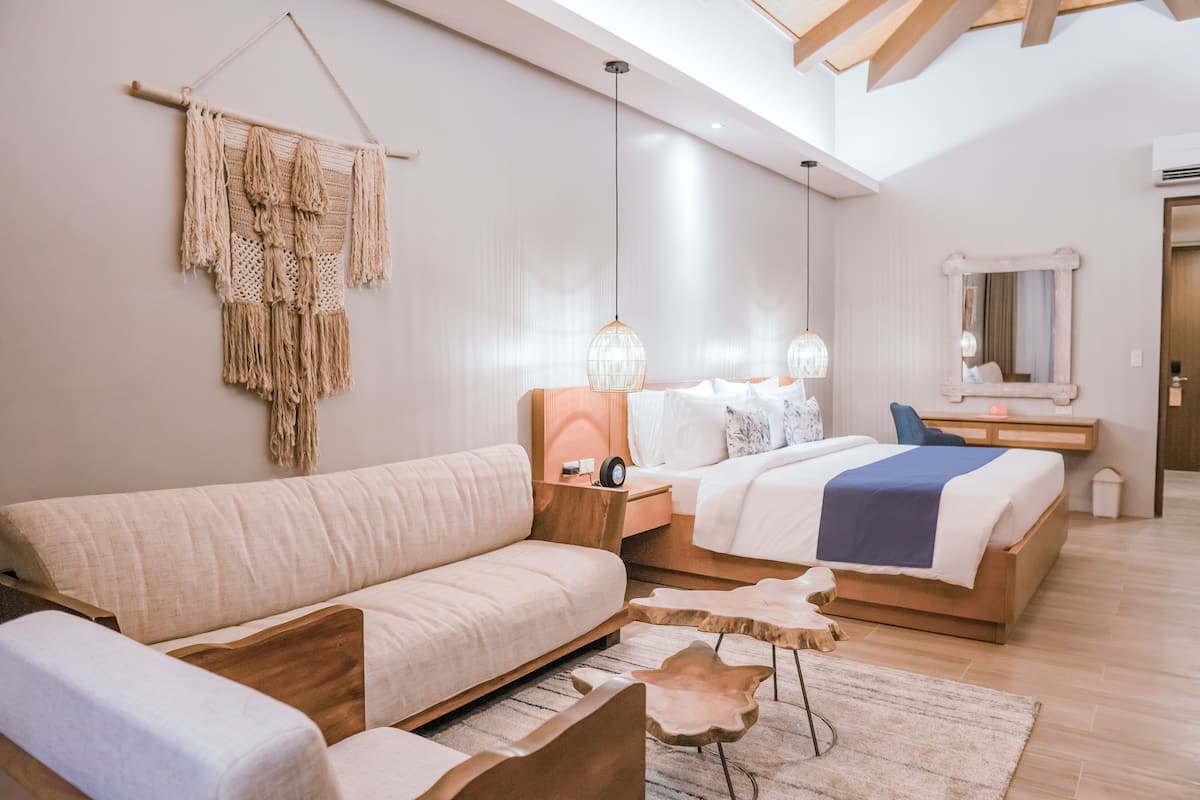 Un dormitorio moderno con una cama grande, un sofá, un escritorio y un adorno de macramé colgante.