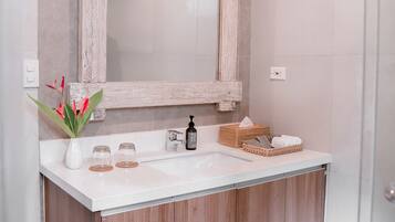 A modern bathroom with a wooden vanity, a large mirror, and a vase with flowers.