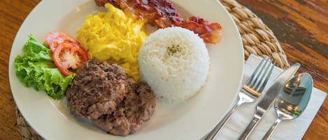 Un plato con huevos revueltos, tocino, arroz, una hamburguesa y una ensalada.