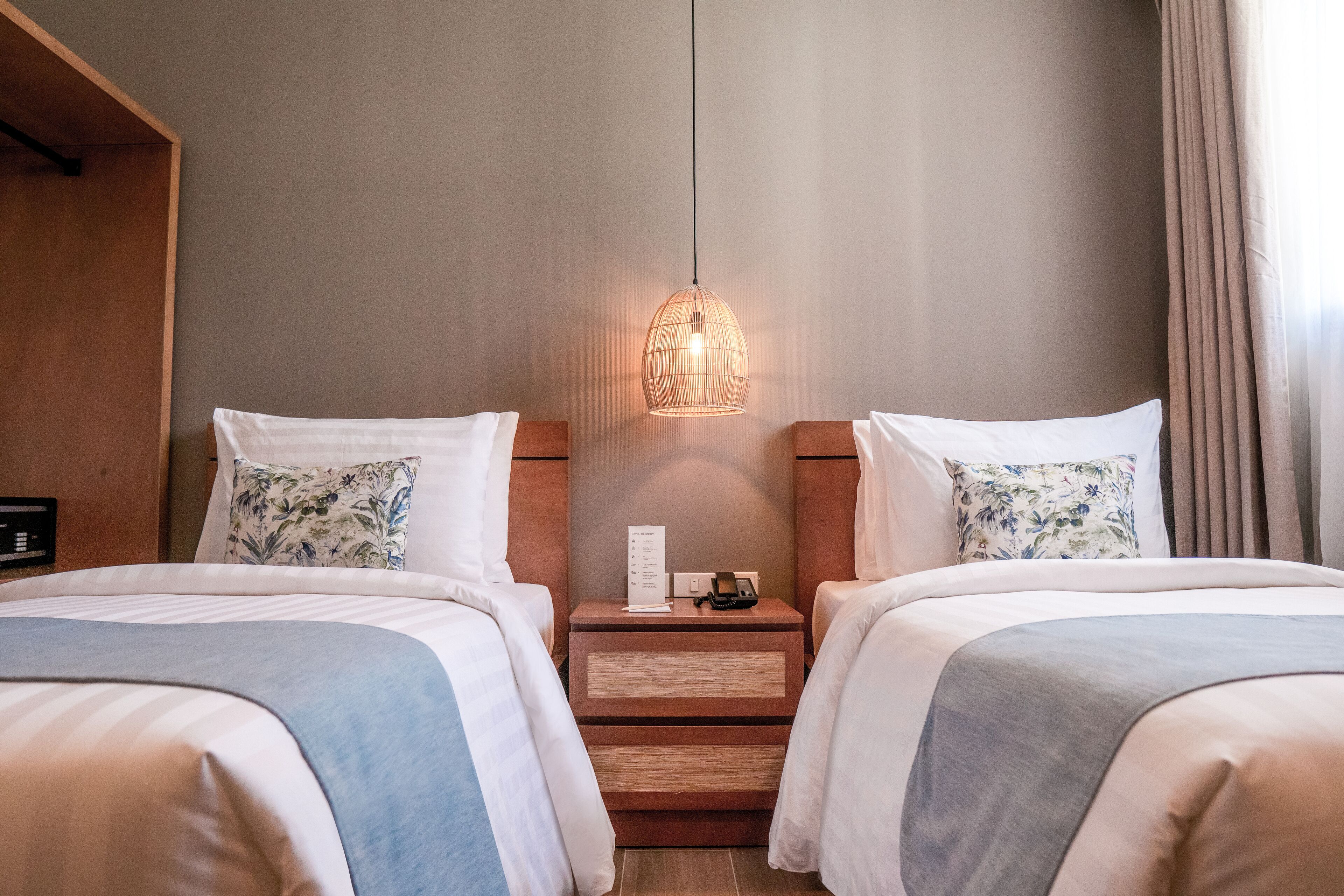 Una habitación de hotel con dos camas, una mesita de noche con teléfono y lámpara, y un cabecero de madera.