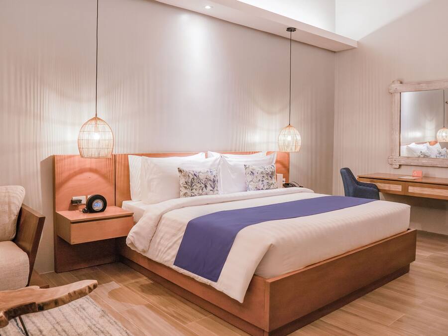 A modern hotel room with a large bed, wooden headboard, bedside tables, a desk, and a mirror.