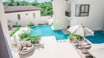 A rooftop pool area with lounge chairs, umbrellas, and a view of surrounding greenery.