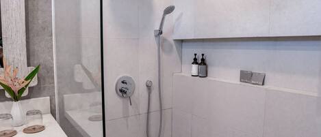 A modern bathroom with a glass shower enclosure, a white sink with a vase of flowers, and a shelf with toiletries.