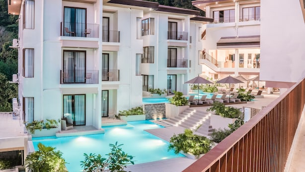 Un hotel de varios pisos con piscina, mobiliario exterior y balcones.