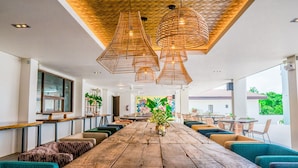 Un comedor amplio con una larga mesa de madera, diversas opciones de asiento y lámparas de mimbre colgantes.