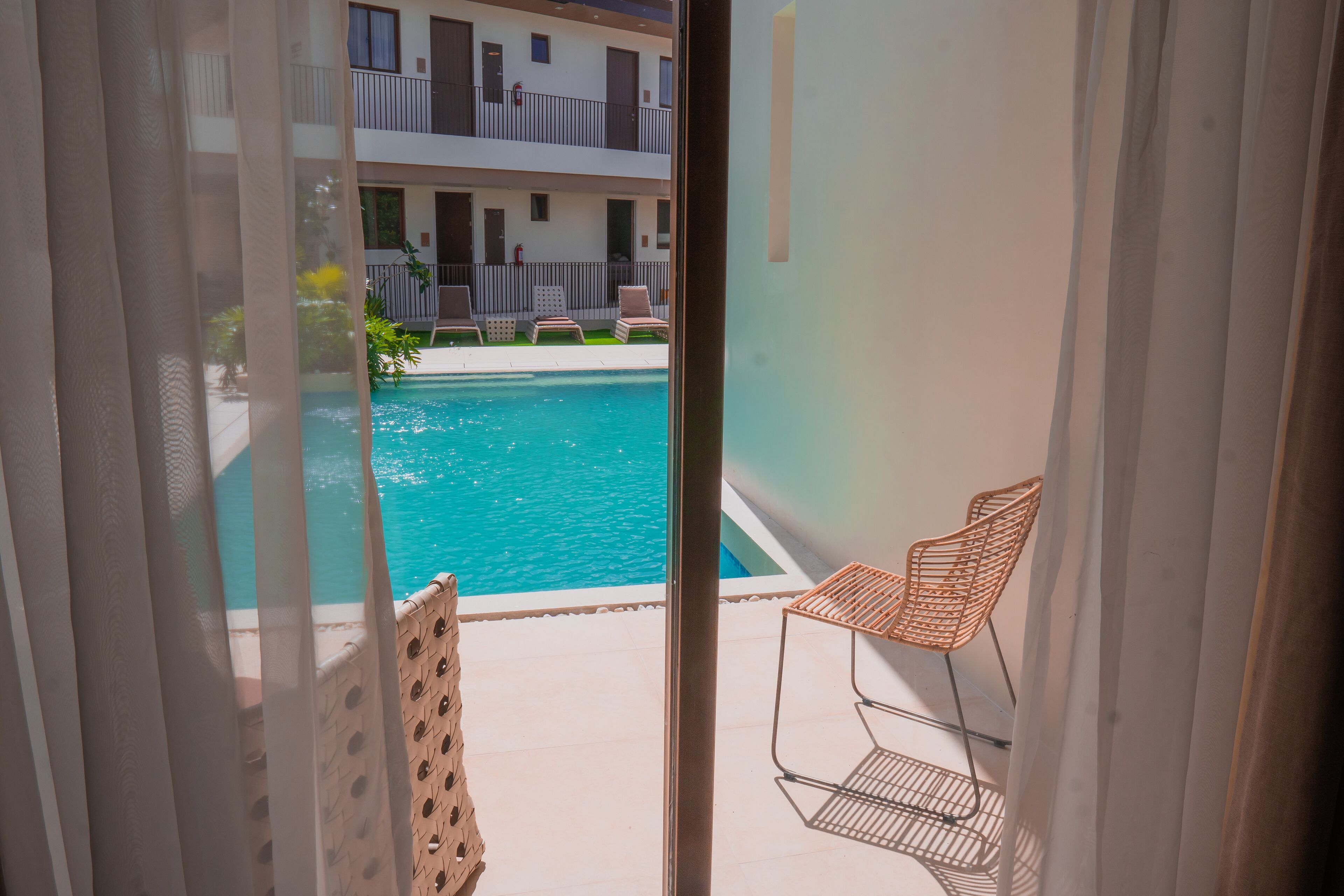On aperçoit, à travers une porte vitrée, un espace piscine avec une chaise et une petite table.