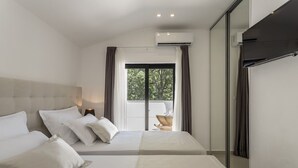 Una habitación de hotel moderna con dos camas, un ventanal con cortinas, un equipo de aire acondicionado y vistas a zonas verdes.