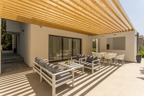 A modern outdoor patio with a wooden pergola, a sofa set, and a dining table with chairs.