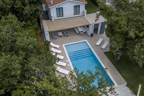 An aerial view of a modern house with a swimming pool, surrounded by trees.