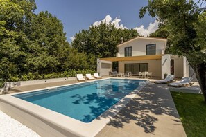 A modern house with a swimming pool, sun loungers, and a patio area.
