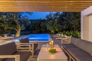 A modern outdoor pool area with lounge chairs and a table, surrounded by trees. - Villa Ventura with a private heated pool, superfast broadband, gym (Srinjine)