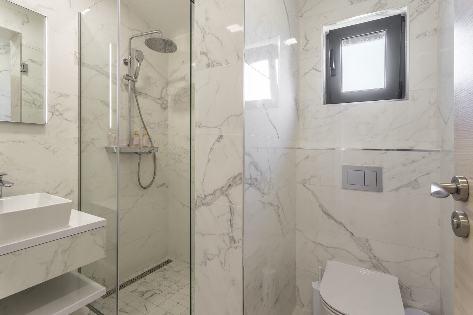 Un baño moderno con ducha envuelta en vidrio, lavamanos blanco y retrete.