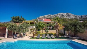 A swimming pool with lounge chairs, a covered patio, and a mountain backdrop. - VILLA PAULA, 7 bedrooms, heated 36sqm private pool, Jacuzzi, Gym and sea views (Kastel Gomilica)