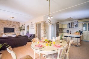 A modern living room with a TV, sofa, and dining area with a table set for four.