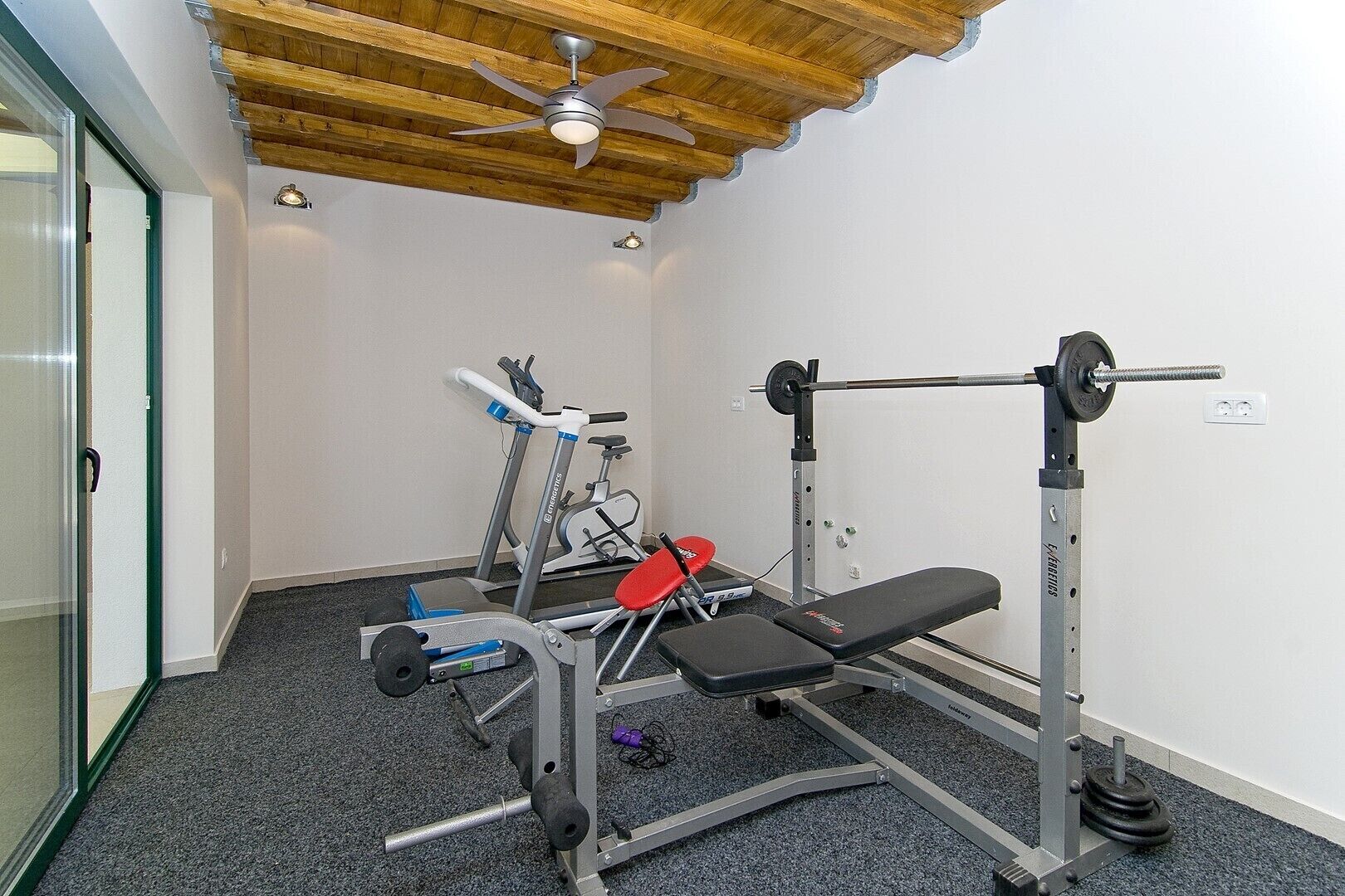 Une petite salle de sport équipée d’un tapis de course, d’un banc de développé couché et d’un banc de musculation.