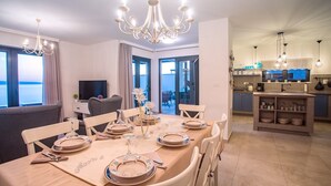 A dining area with a table set for six, a chandelier, and a view of the sea through large windows. - Villa Nano - Private heated 32 sqm infinity pool, a jacuzzi, amazing sea views (Jesenice)