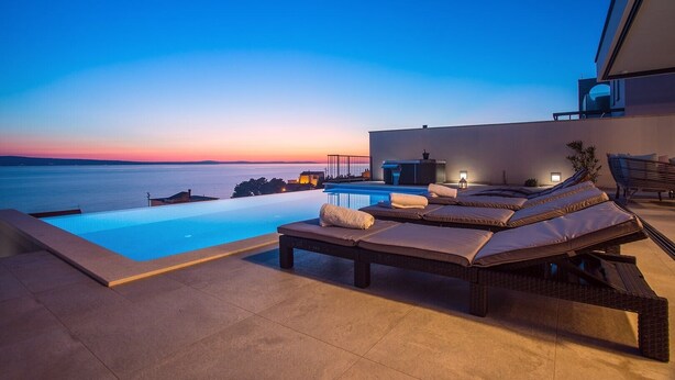 A rooftop infinity pool with lounge chairs and a bar area, overlooking a body of water at sunset. - Villa Nano - Private heated 32 sqm infinity pool, a jacuzzi, amazing sea views (Jesenice)