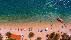 An aerial view of a beach with clear turquoise water, people swimming, and beach umbrellas. - Villa Nano - Private heated 32 sqm infinity pool, a jacuzzi, amazing sea views (Jesenice)