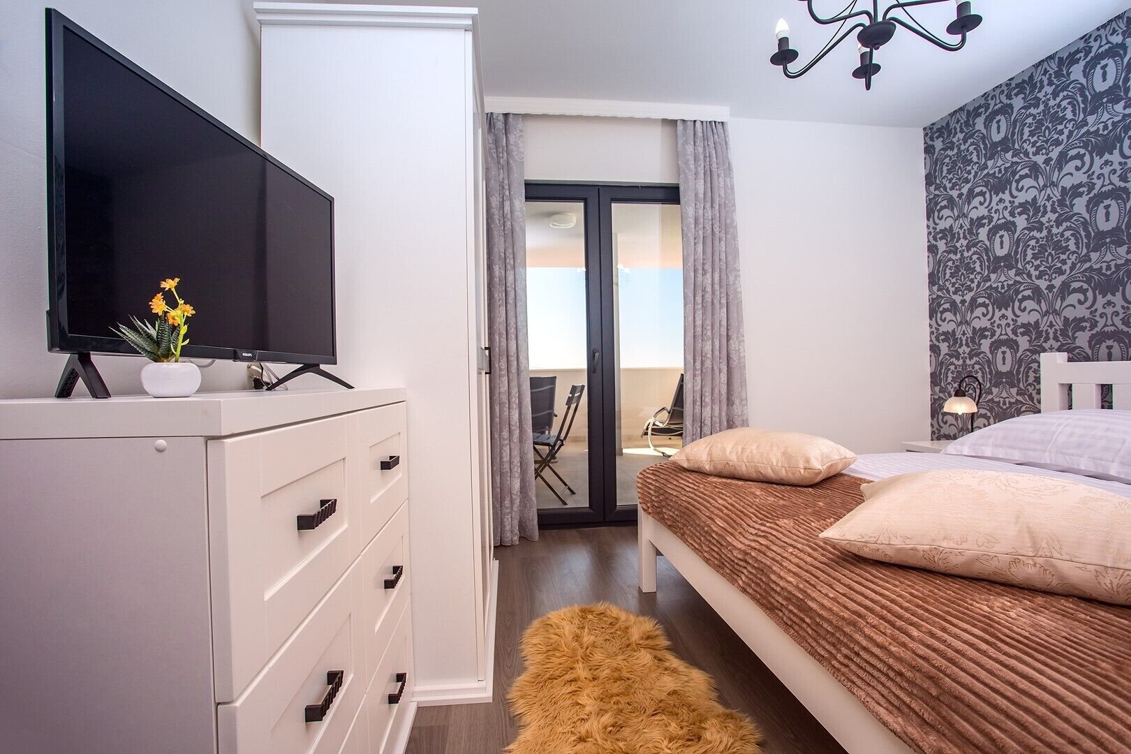 A modern bedroom with a TV on a dresser, a bed with a fluffy rug, and a patterned wall.