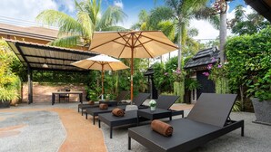 Un espace de détente extérieur avec des fauteuils en osier, un coin salon abrité et des parasols.