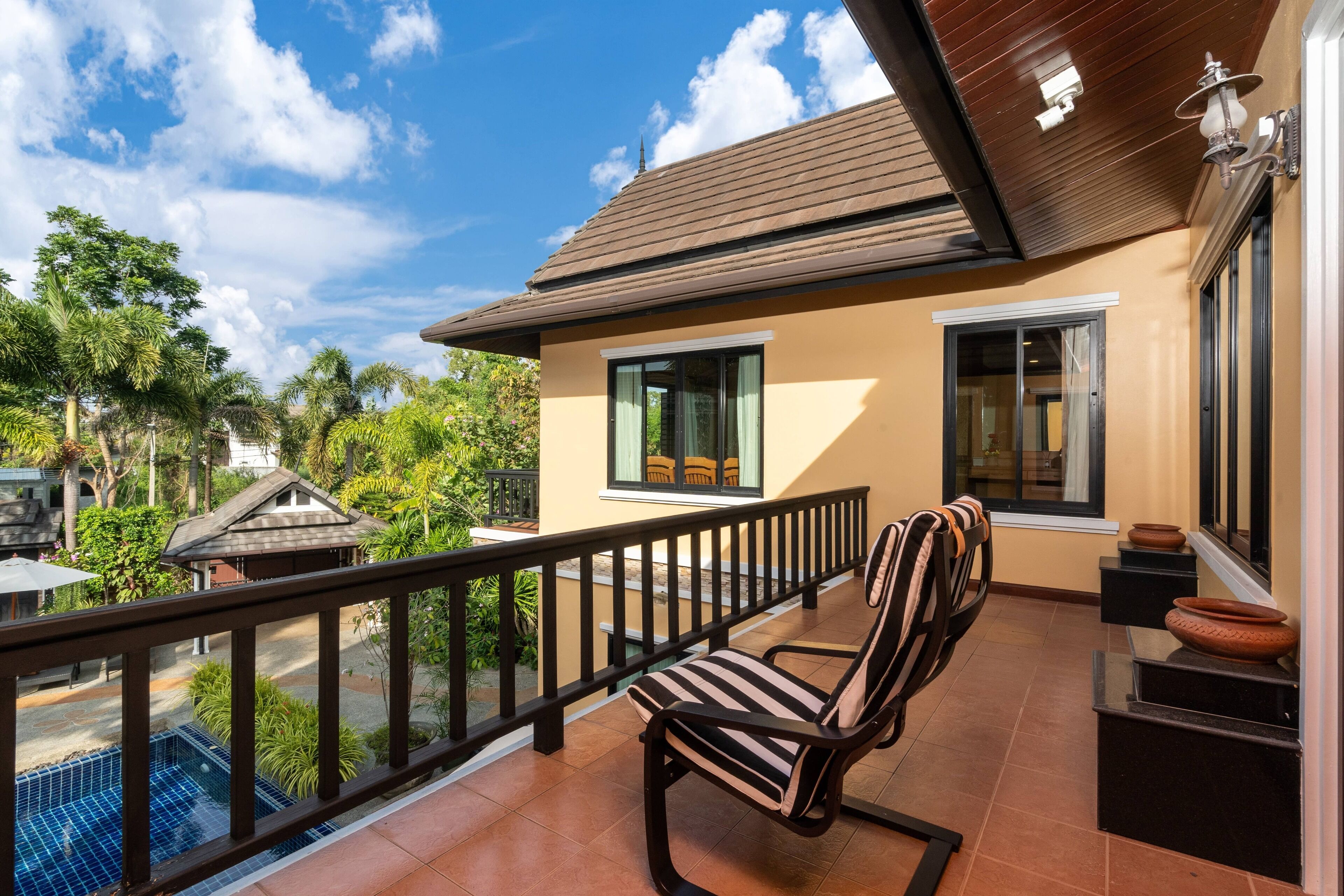 A balcony with a view of a swimming pool, a chair, and a small table with a potted plant.