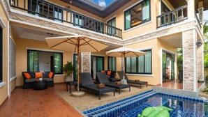 Une maison à deux étages avec une piscine, un espace salon extérieur et un balcon.