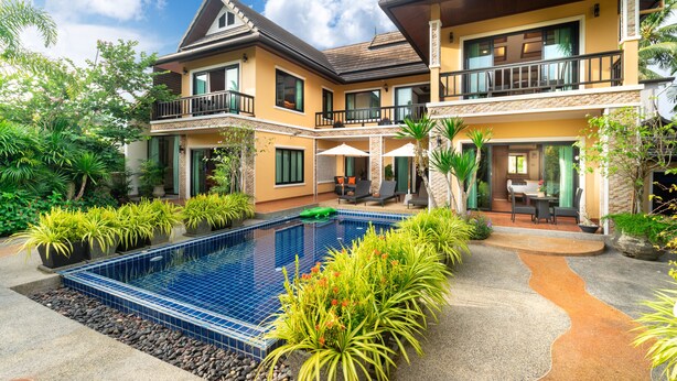 Une maison à deux étages avec une piscine, du mobilier d’extérieur et une végétation luxuriante.