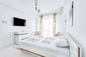 Una camera da letto moderna con un letto, una TV, una cassettiera e una finestra con tende.