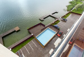 Vista aerea di una piscina con bordo in legno, parcheggio nelle vicinanze e area verde.
