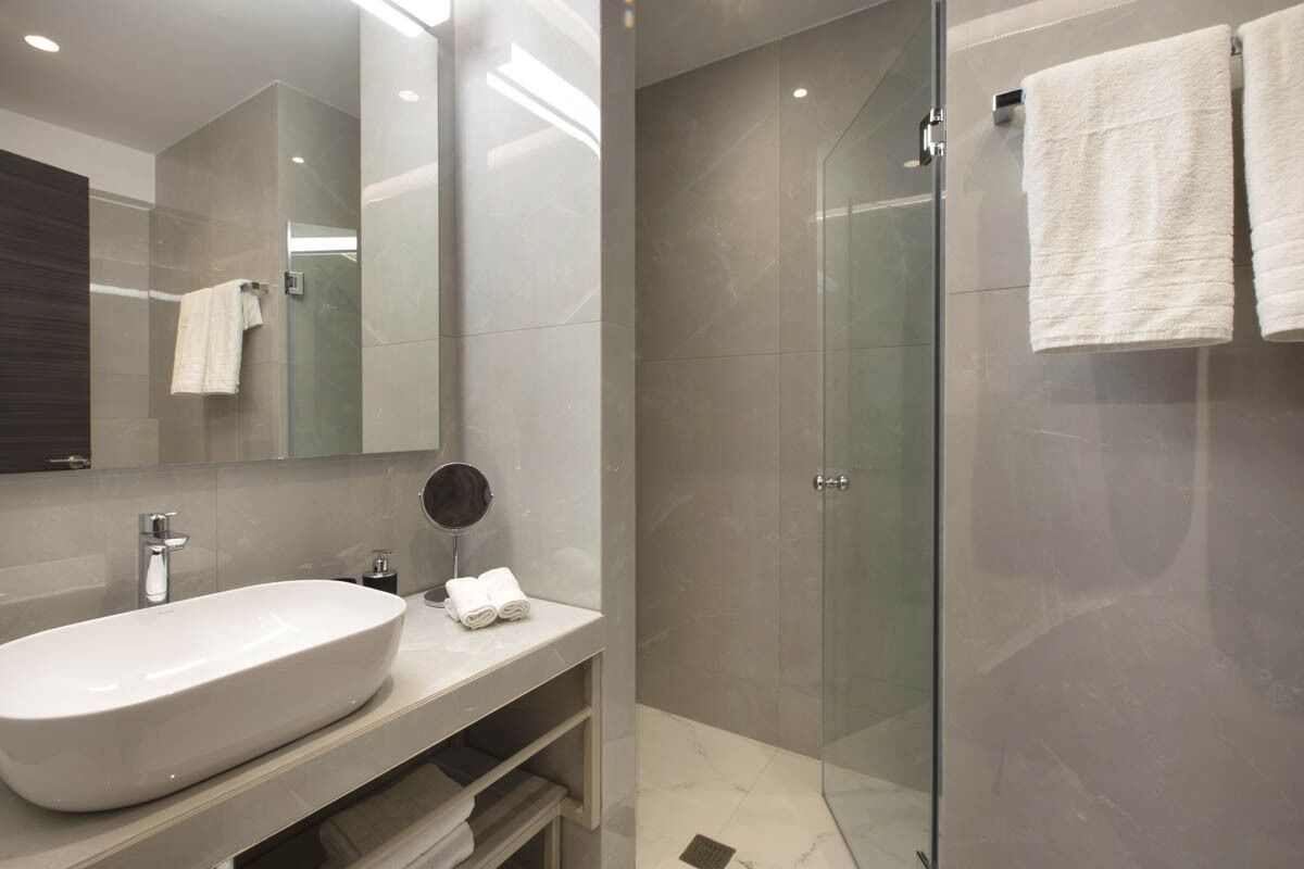 Ein modernes Badezimmer mit einem großen weißen Waschbecken, einer gläsernen Dusche und einem Spiegel mit rundem Rahmen.