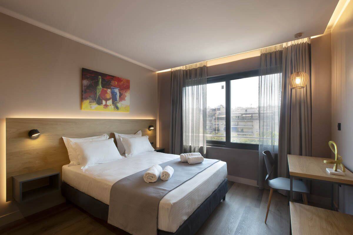 A modern hotel room with a large bed, a desk, and a view of the city through the window.