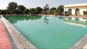 Piscina com espreguiçadeiras e um edifício ao fundo.