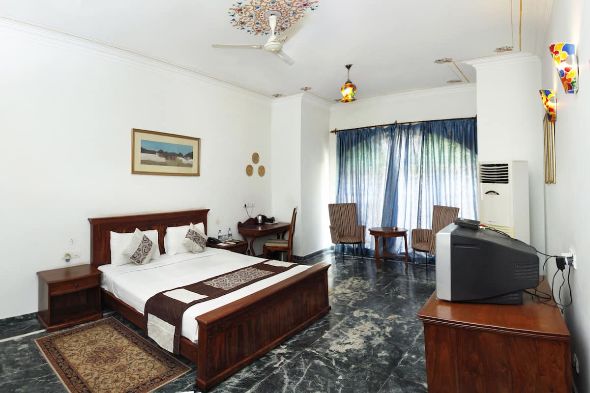 A hotel room with a large bed, a desk, a television, and a ceiling fan.