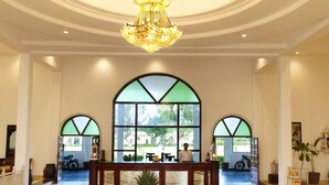Um hall com balcão de recepção, grandes janelas em arco, um candelabro e piso de azulejos.