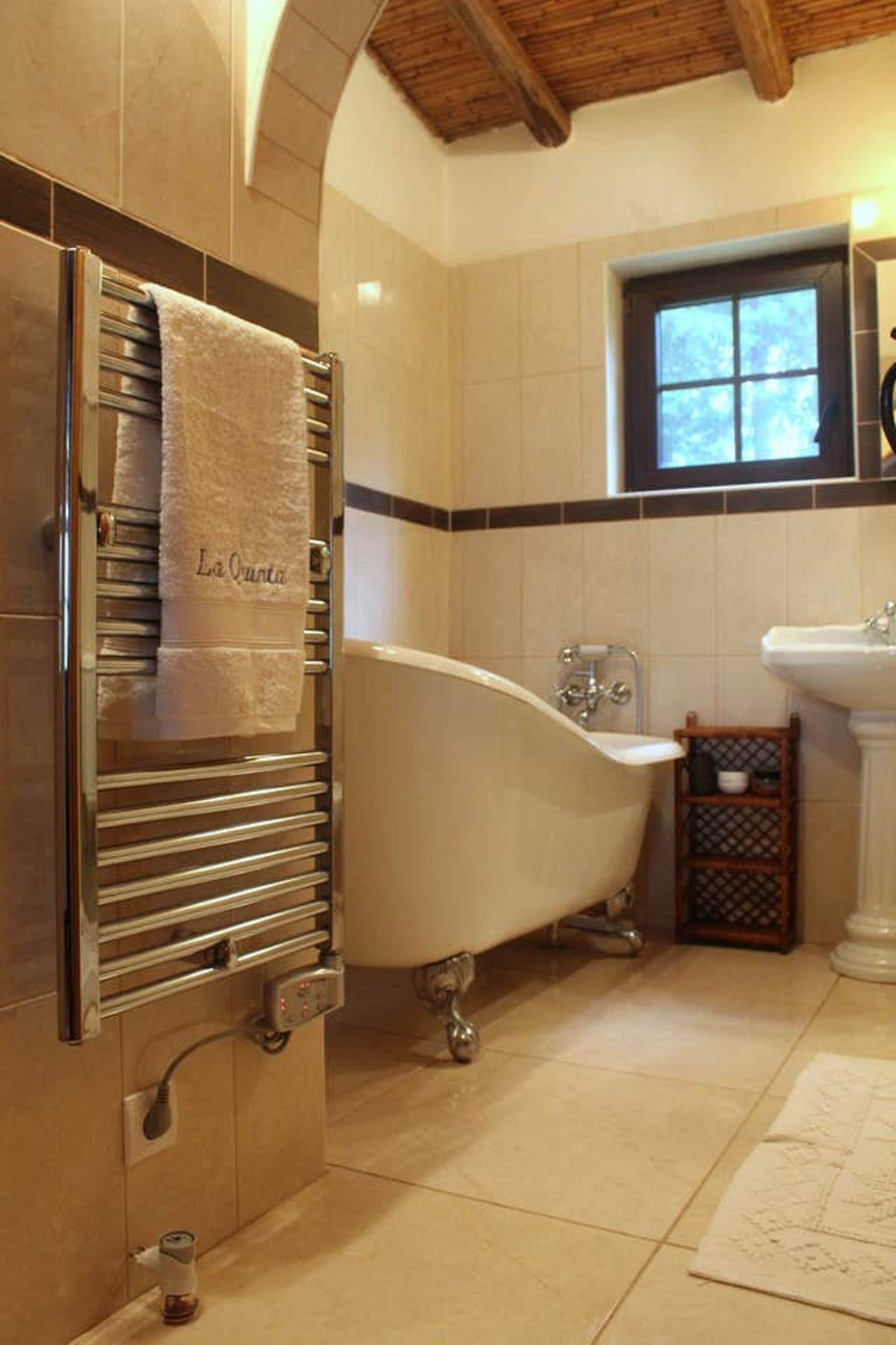 A bathroom with a freestanding bathtub, a towel rack with a towel, a sink, and a window.
