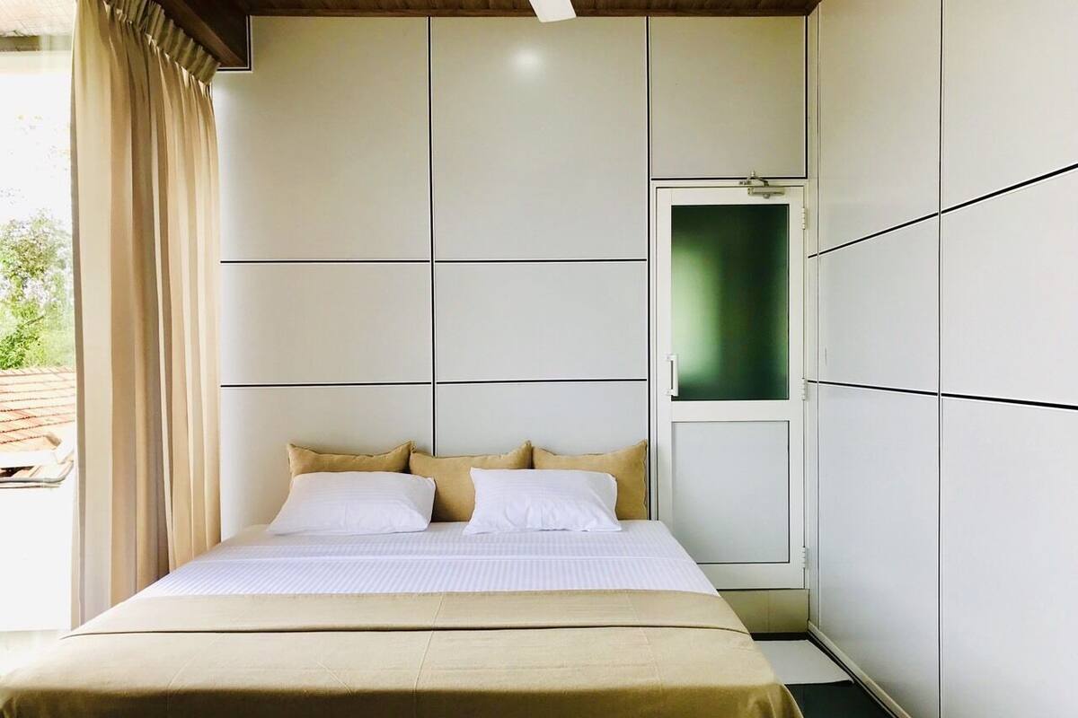 Ein modernes Schlafzimmer mit einem Bett, beigefarbener Bettwäsche und Blick auf Grünfläche.
