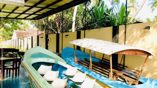 A boat with white cushions and a blue cover, docked at a poolside area with a covered seating area and a wall with a small window. - Tramonto Lagoon Resort (Seeduwa - Katunayake)