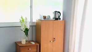 A wooden wardrobe with a small bedside table beside it, a vase with white flowers, and a kettle on top of the wardrobe. - Tramonto Lagoon Resort (Seeduwa - Katunayake)