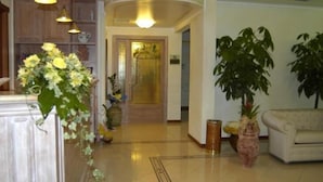 A spacious lobby with a reception desk, a sofa, and potted plants. - Hotel Terra di Gallura (Budoni)