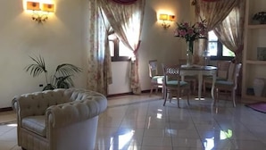 A spacious living area with a plush sofa, a dining table with chairs, and decorative wall sconces. - Hotel Terra di Gallura (Budoni)