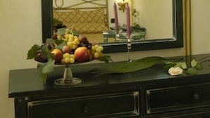A mirror with a black frame, a black desk with drawers, and a vase with fruit and flowers. - Hotel Terra di Gallura (Budoni)