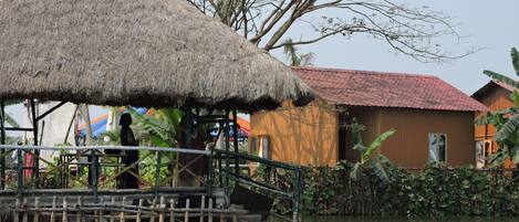 A thatched-roof structure with a wooden house in the background.